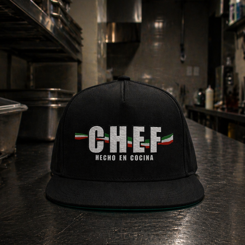 Black cap with 'CHEF hecho en cocina' text on a metallic surface in a kitchen setting